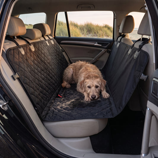 Quilted black seat cover fitted across the rear bench of an estate car, with a wet sandy terrier lying on it