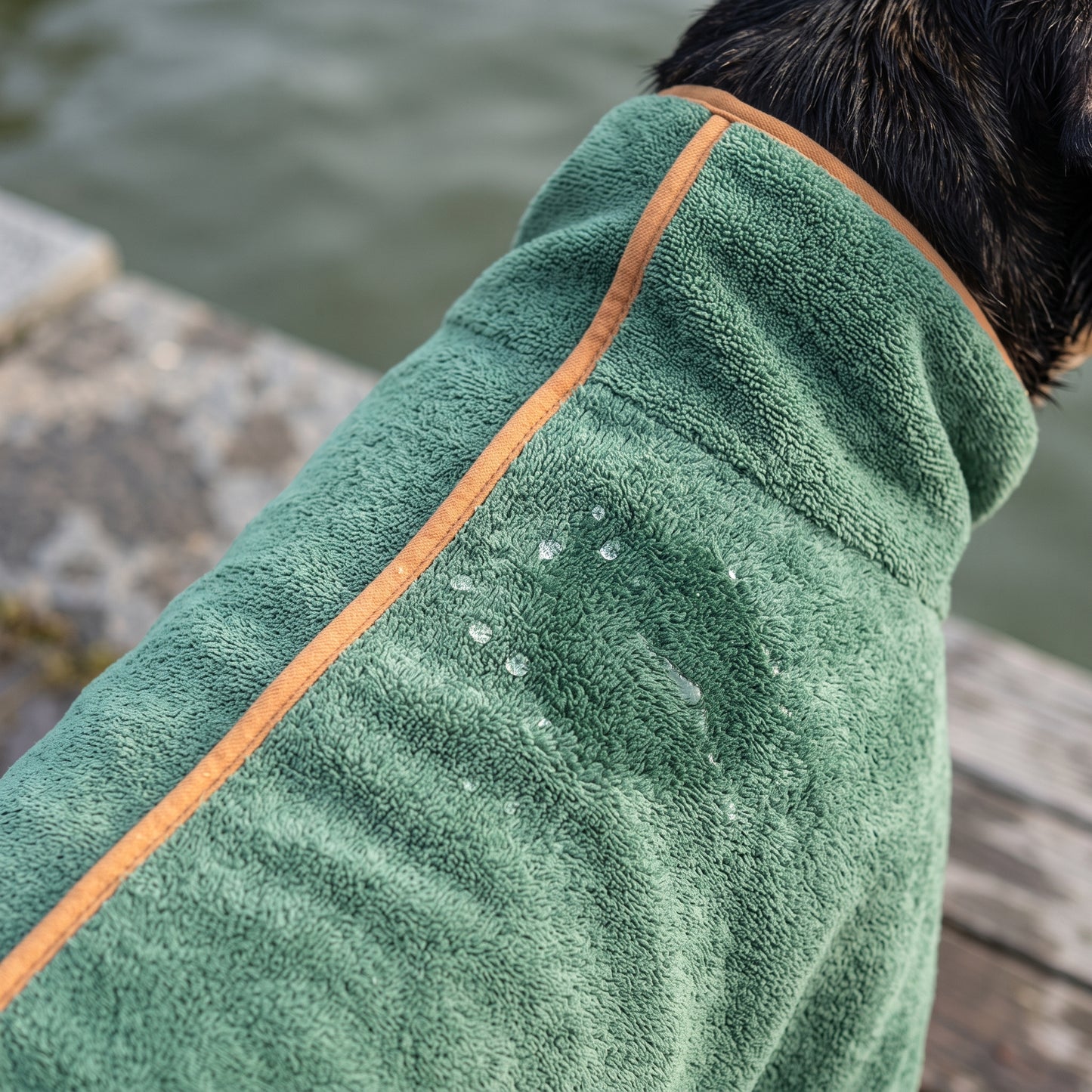 Close-up of the green Dry Dock Robe's microfiber pile with water beaded on the surface and orange trim along the seam.