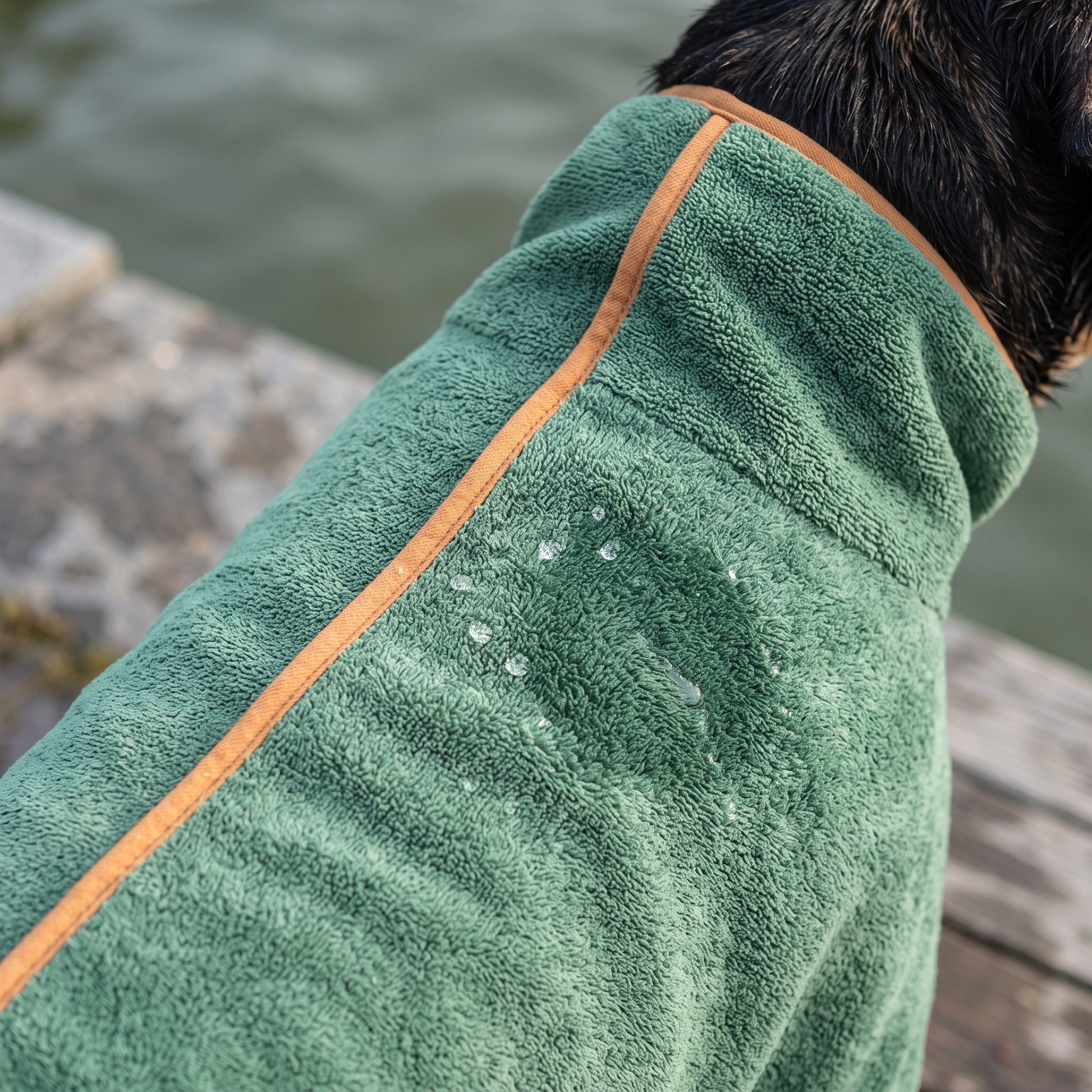 Close-up of the green Dry Dock Robe's microfiber pile with water beaded on the surface and orange trim along the seam.
